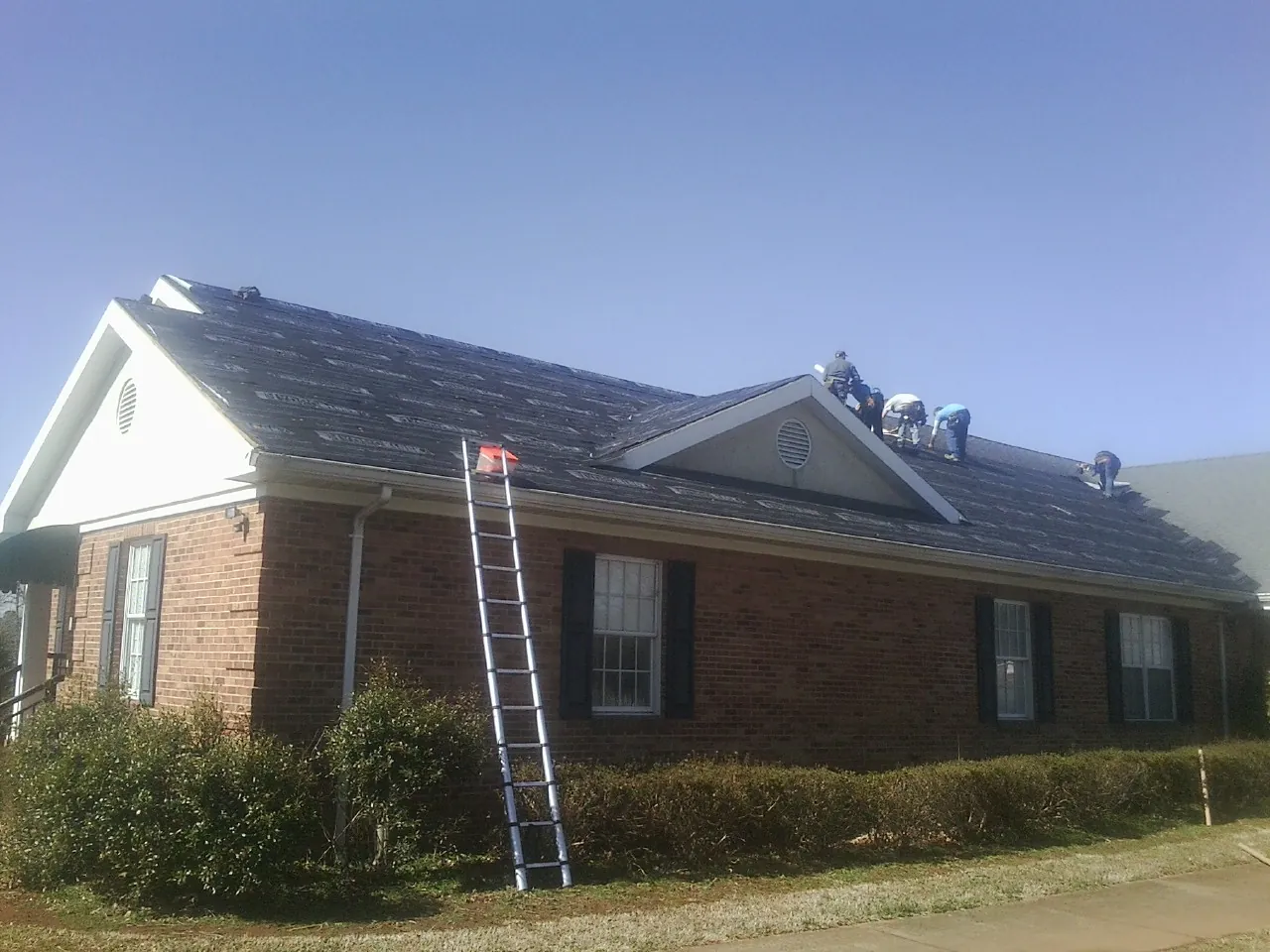 Crew tearing shingles off a brick ranch roof with a ladder set — Emergency Roof Repair work by our crew in Oxnard