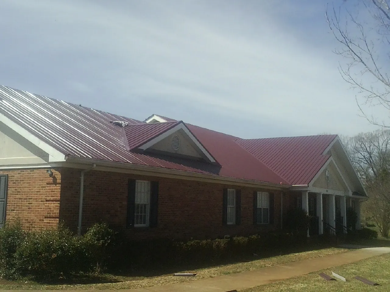 Red metal roof with gabled entries on a long brick building, from a Hail Damage Roof Repair job in Oxnard